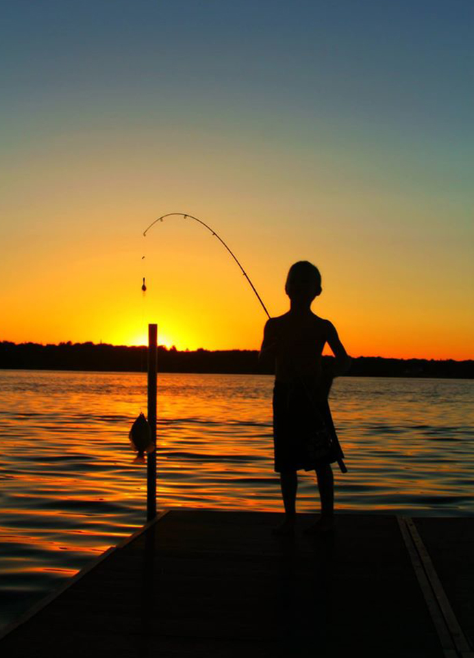 Boy fishing from dock at sunset